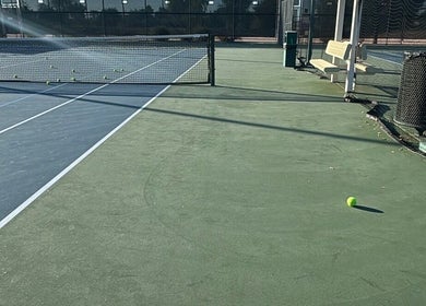 Empty tennis courts at Racket & Paddle Club, Gilbert, Arizona, US, with scattered tennis balls under clear skies.