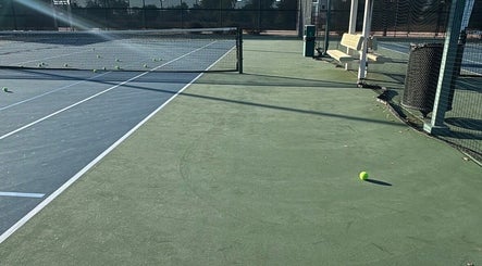 Empty tennis courts at Racket & Paddle Club, Gilbert, Arizona, US, with scattered tennis balls under clear skies.