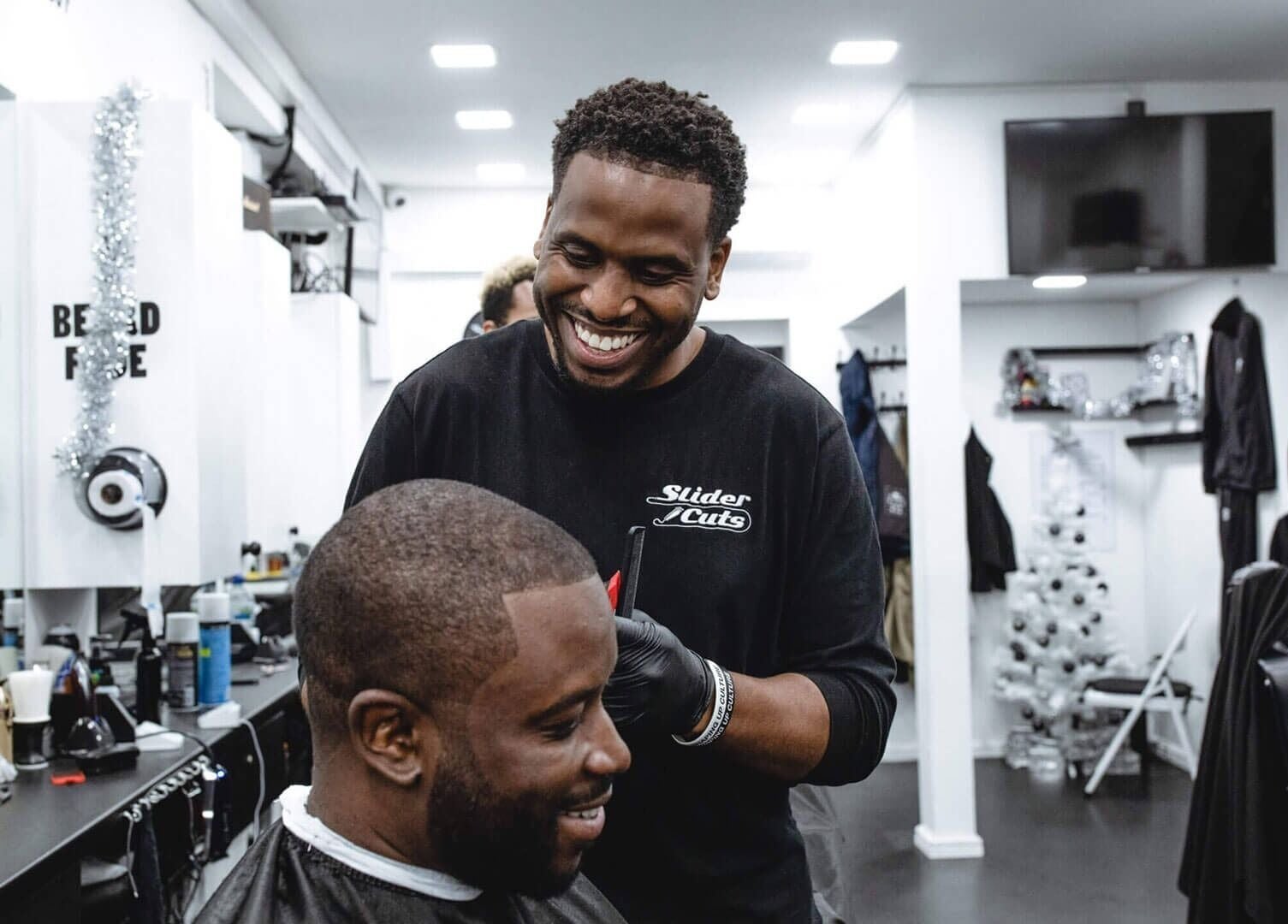 Expert barber at SliderCuts in London, England, GB, offering a modern haircut to a smiling client.