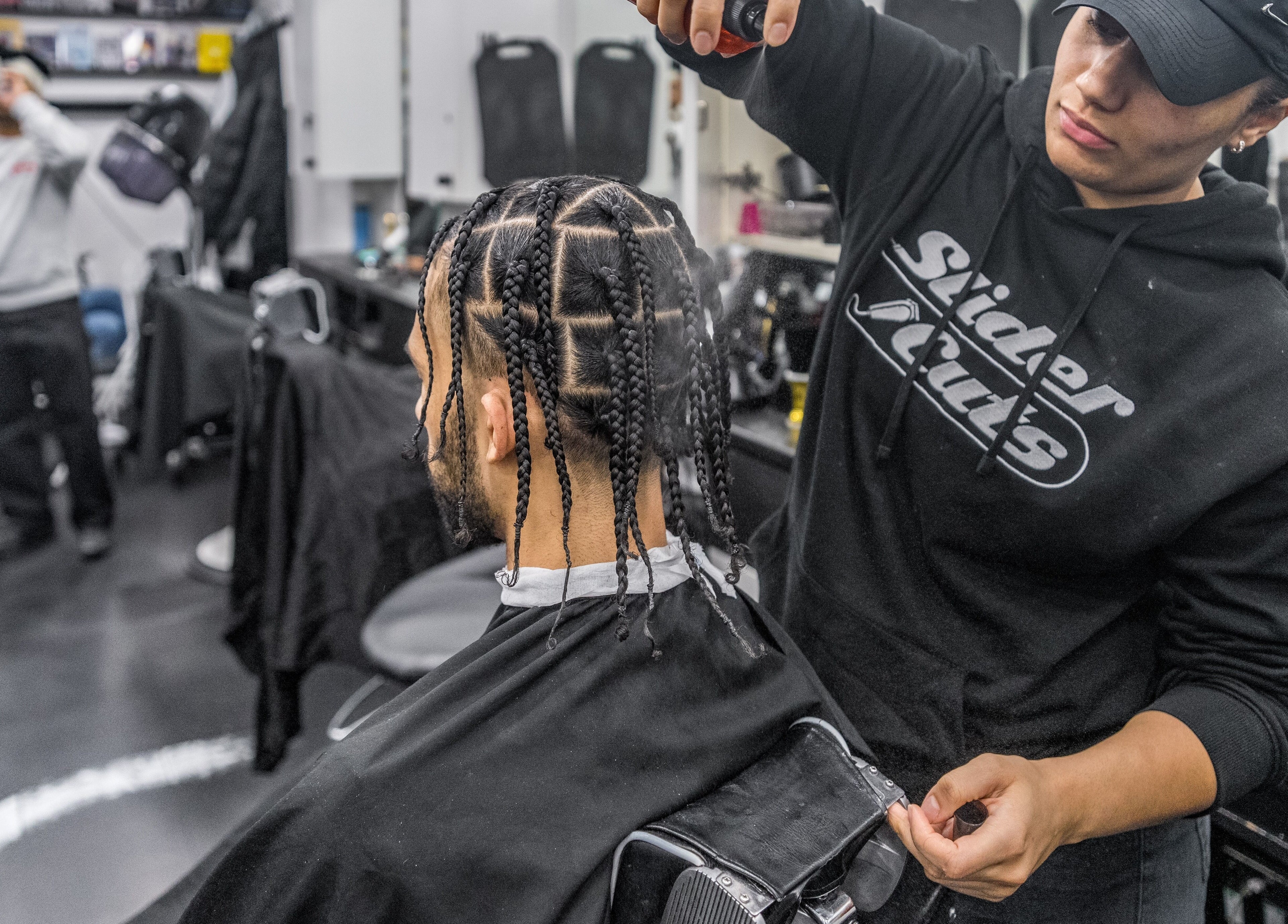 Stylist at SliderCuts in London, England, GB, expertly braiding a client's hair in a modern salon setting.