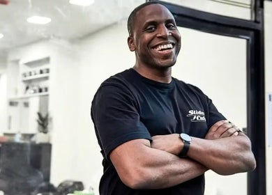 Barber at SliderCuts - Black Eats Fest in London, England, GB, smiling outside a busy salon.