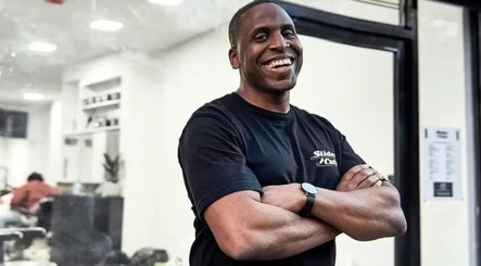 Barber at SliderCuts - Black Eats Fest in London, England, GB, smiling outside a busy salon.