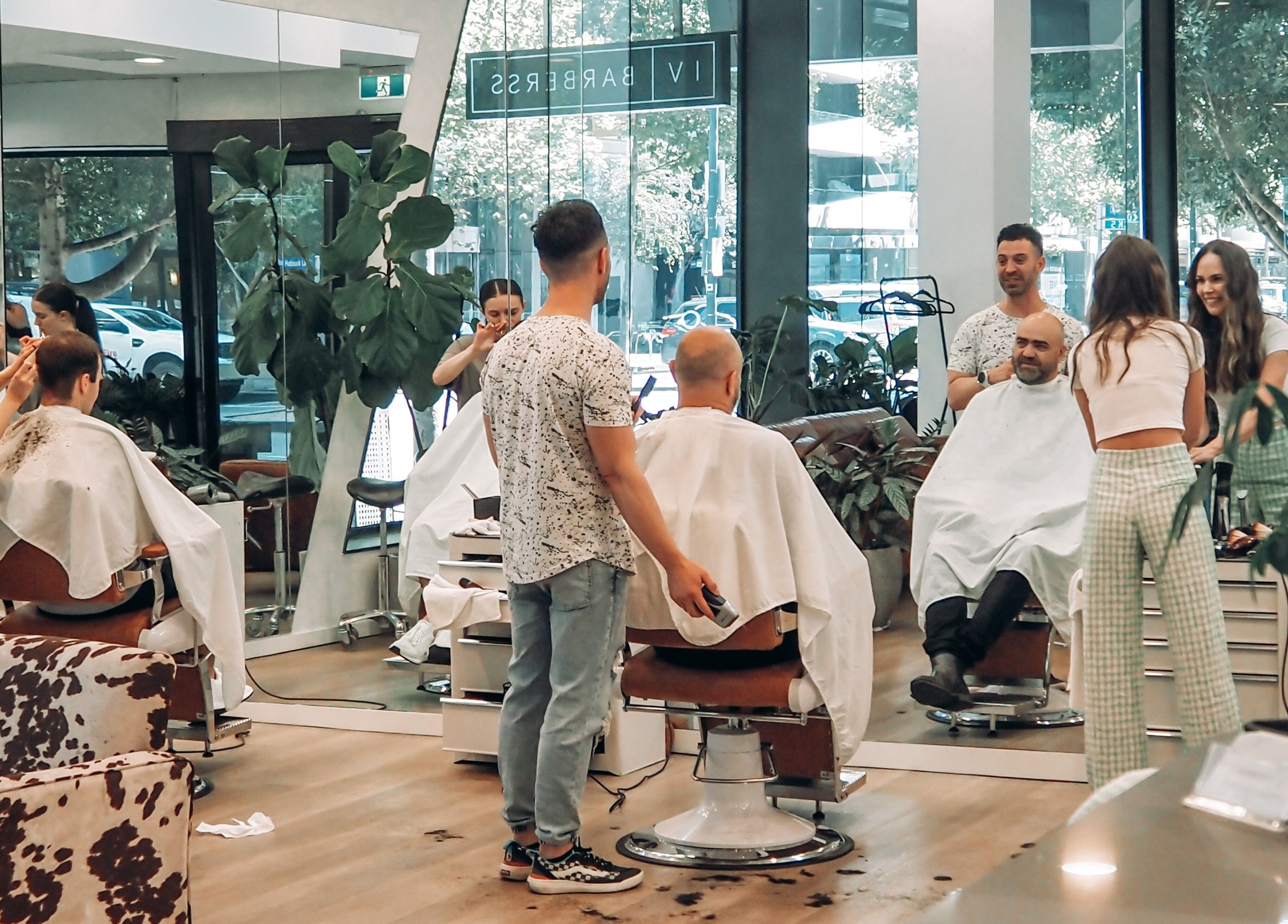 Clients enjoying haircuts at IV Barbers, Melbourne, Victoria, AU. Modern interior and lively atmosphere.