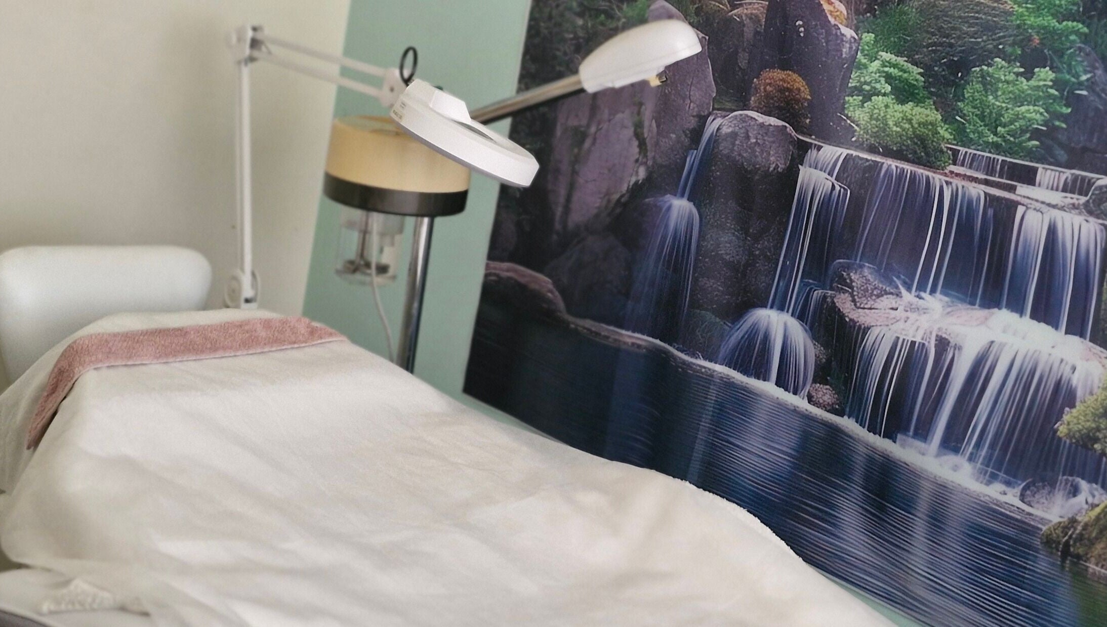 Treatment room at GLOW MASSAGE & AESTHETICS in Hamilton, Waikato, NZ, with serene waterfall mural.