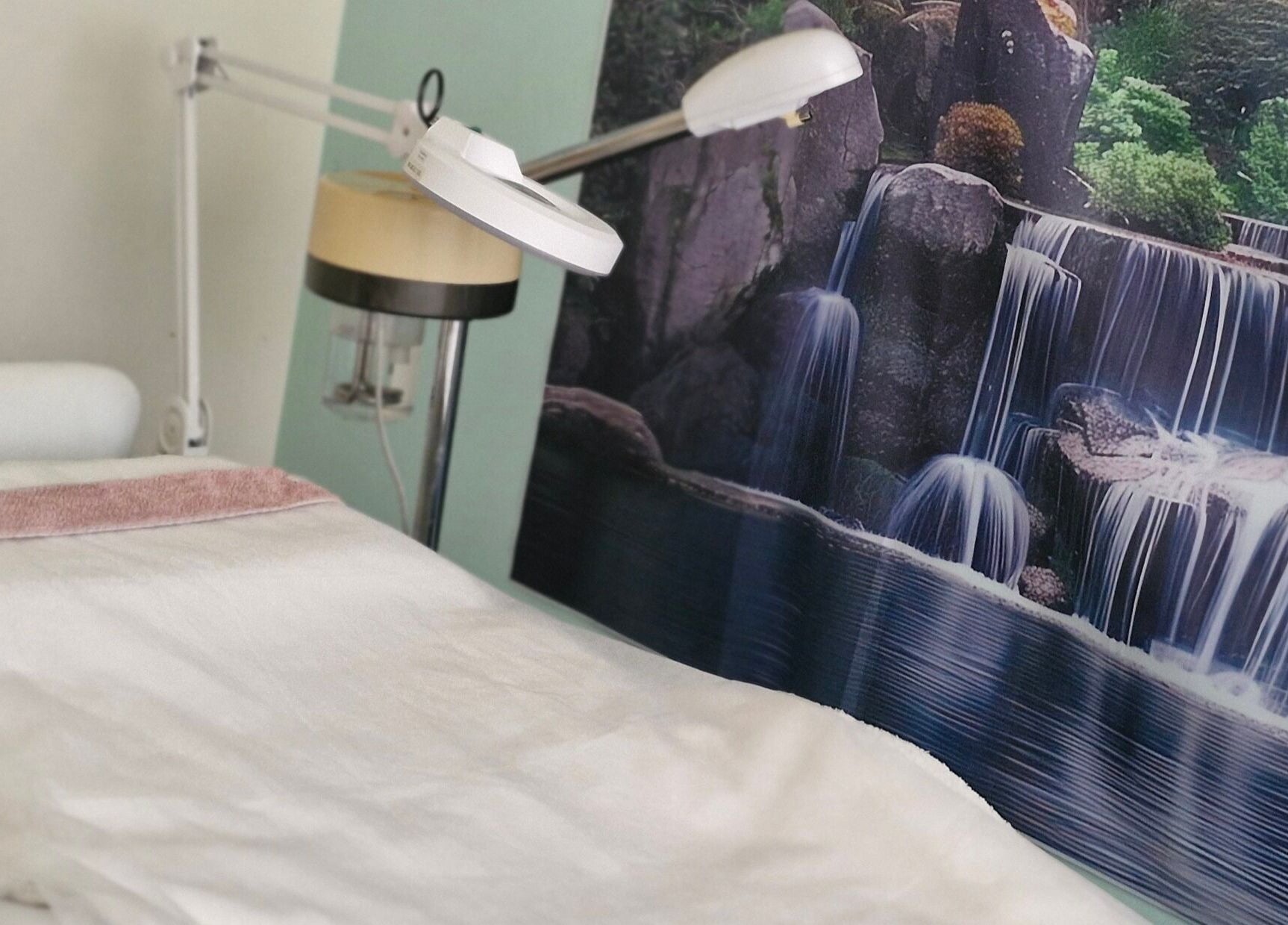 Treatment room at GLOW MASSAGE & AESTHETICS in Hamilton, Waikato, NZ, with serene waterfall mural.