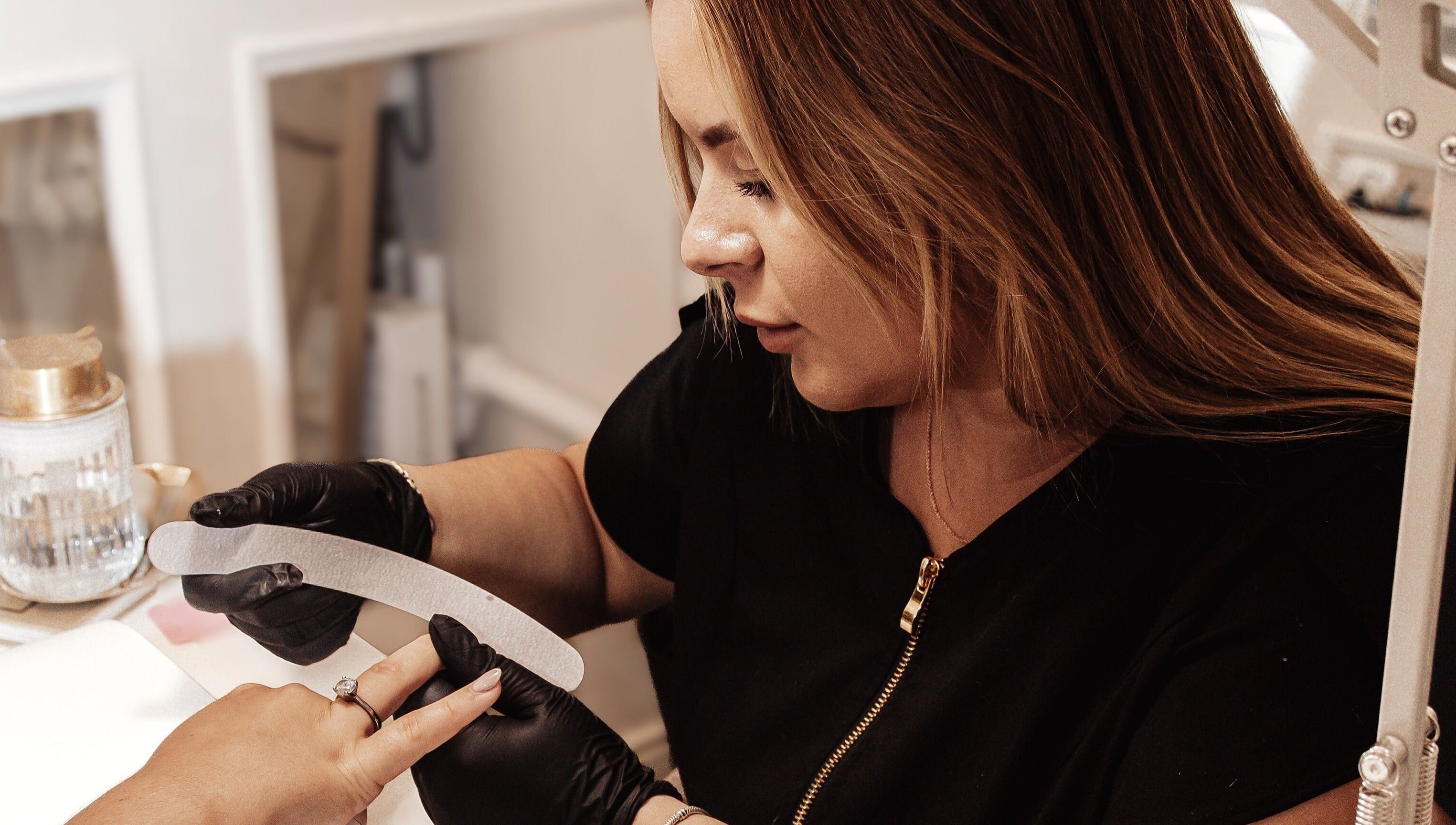 Professional nail technician at Bymolh, Lichfield, England, GB, carefully filing client's nails.