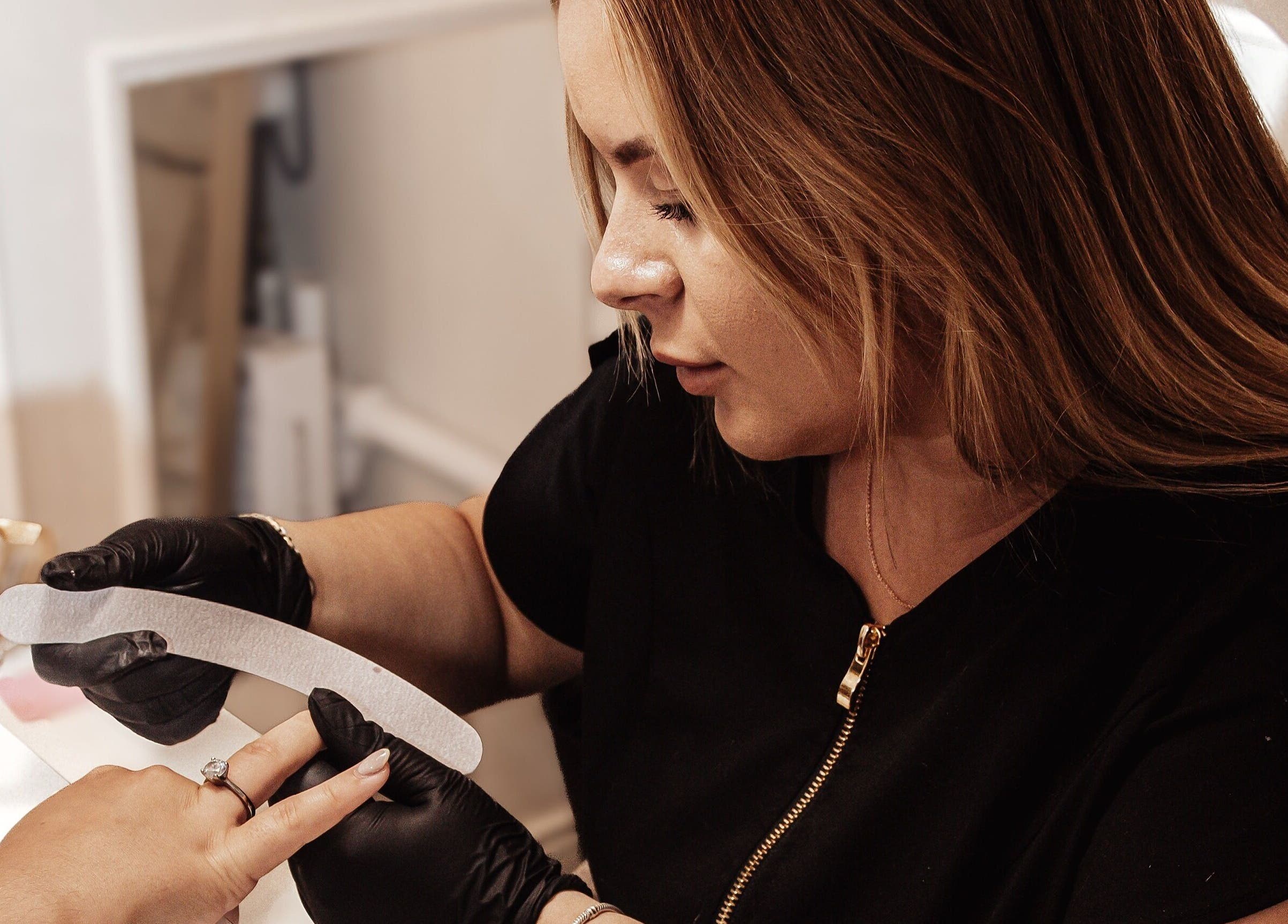 Professional nail technician at Bymolh, Lichfield, England, GB, carefully filing client's nails.