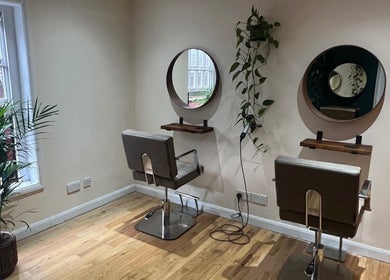 Cozy styling area at Natural Hair Studio, Horsham, England, GB with modern chairs and green plants.