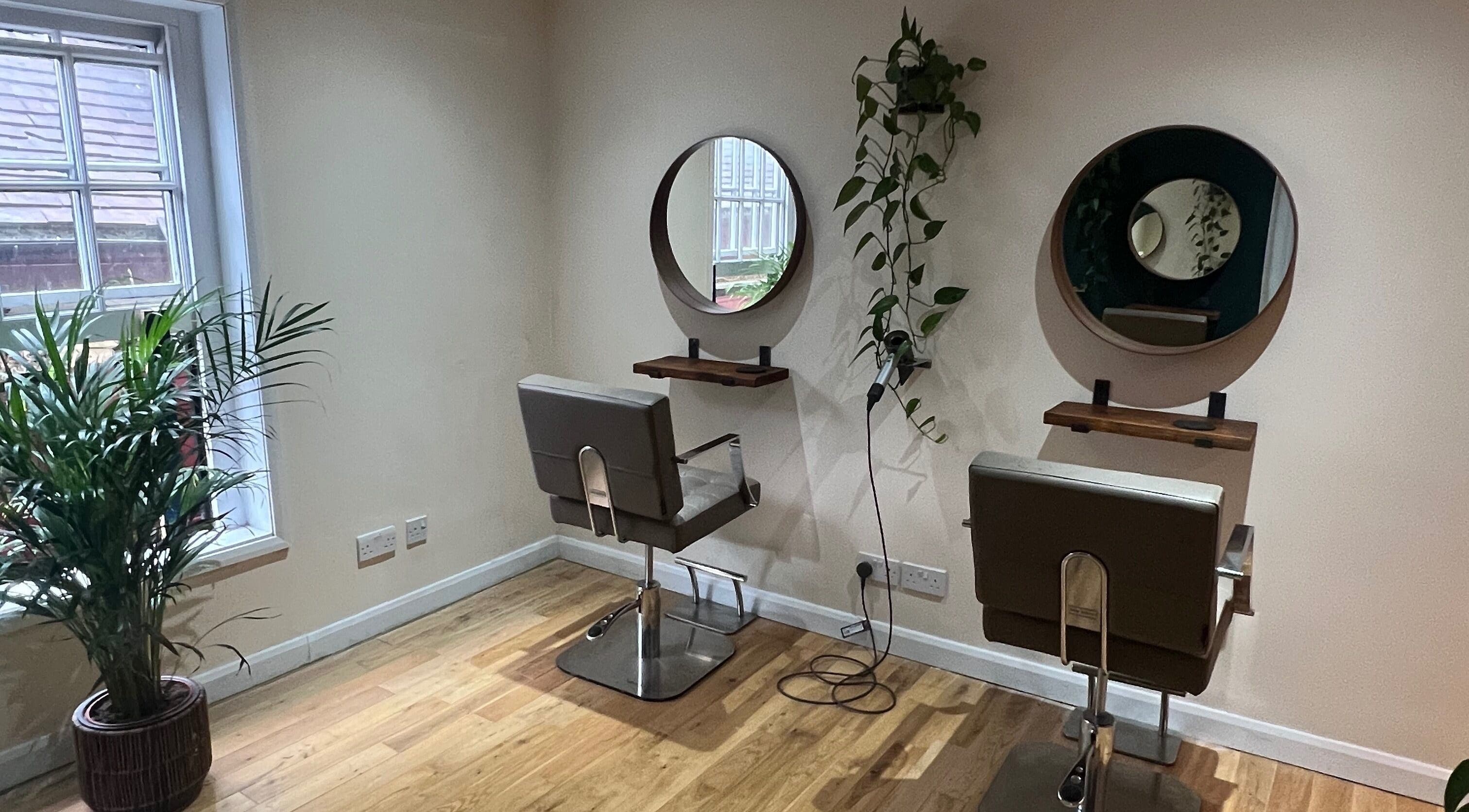 Cozy styling area at Natural Hair Studio, Horsham, England, GB with modern chairs and green plants.