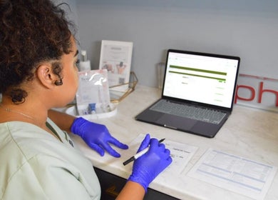 Staff member at Rsg Aesthetics preparing documents at laptop in Cape Town, Western Cape, ZA.