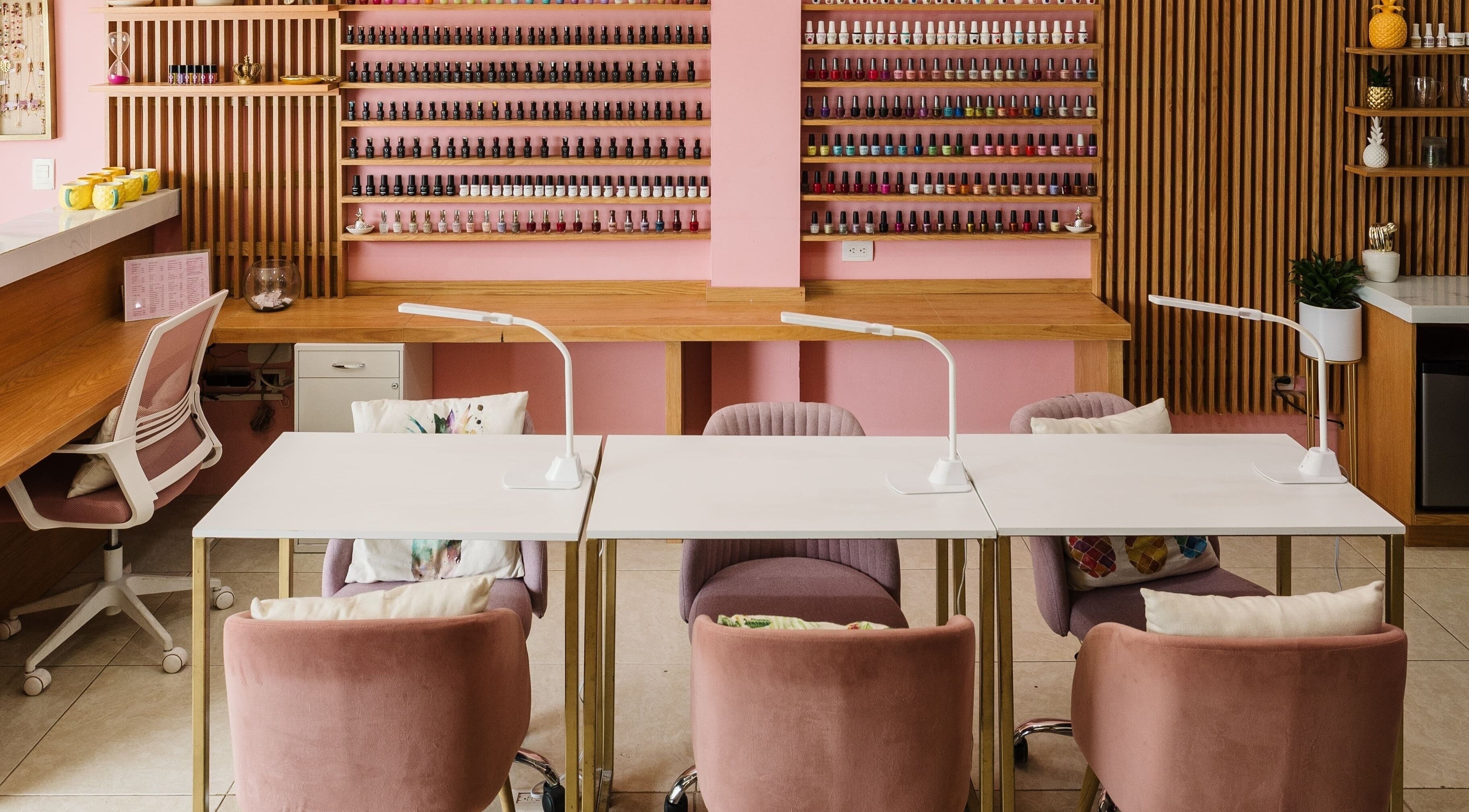 Interior moderno de Piña Nails Room en Mérida, Yucatán, MX, con sillas rosadas y extensa colección de esmaltes.