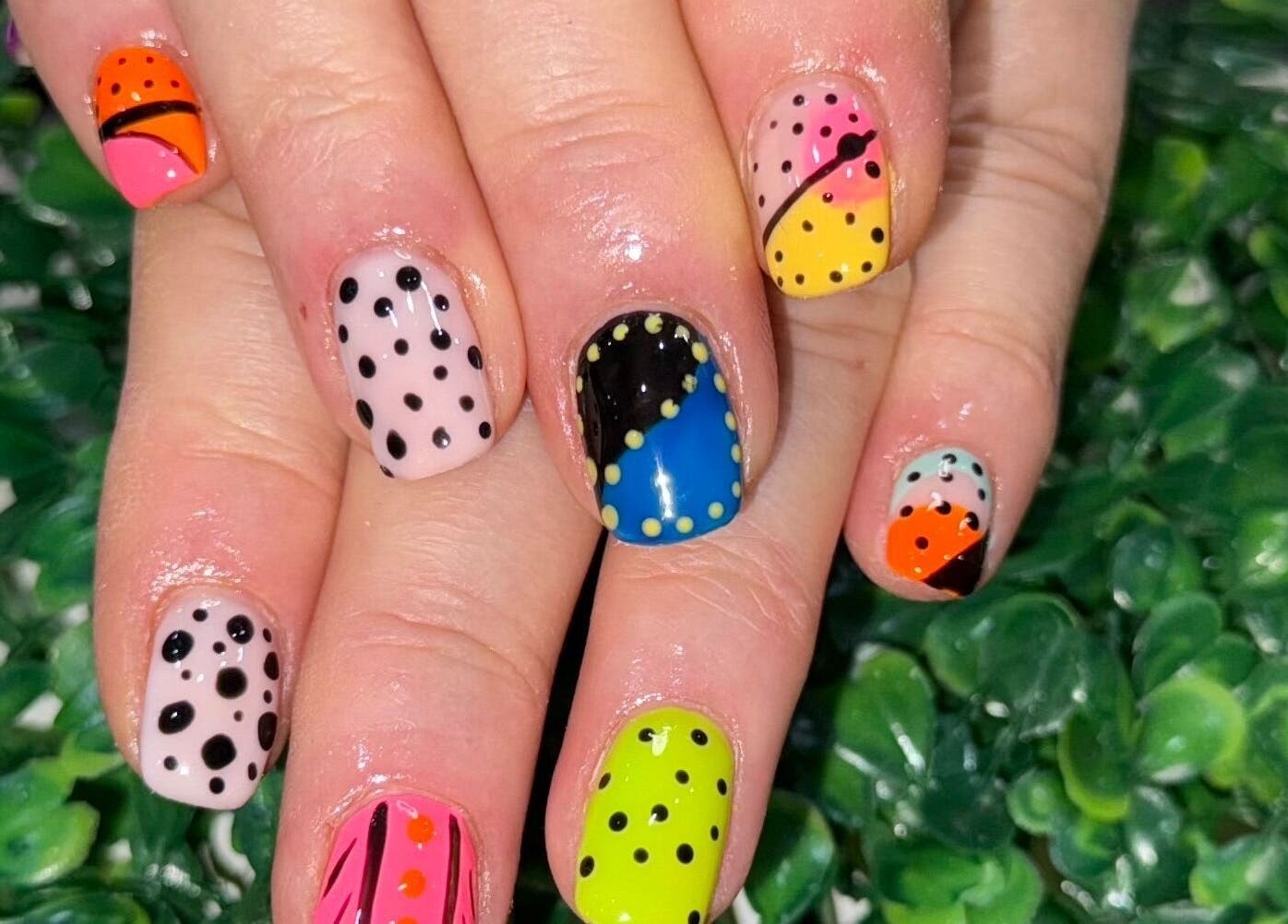 Vibrant polka dot nail art by Nails by Liz, Leabrooks, England, GB, displayed on fresh greenery.