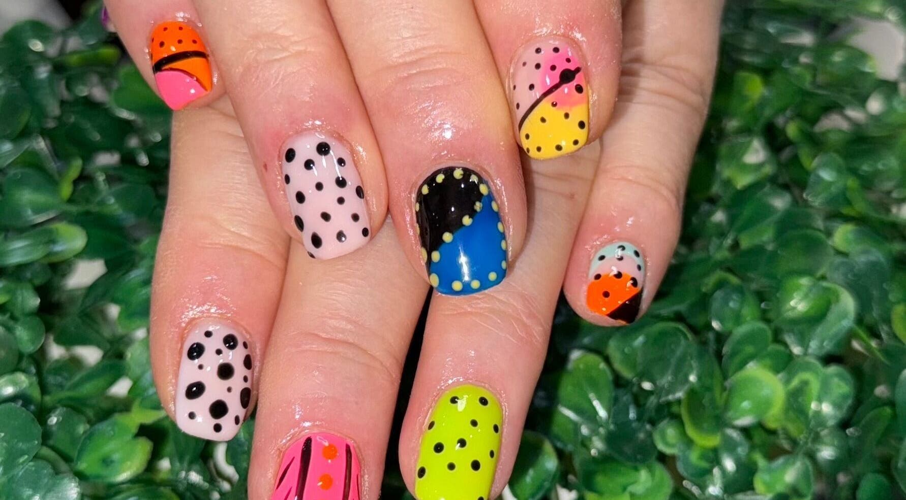 Vibrant polka dot nail art by Nails by Liz, Leabrooks, England, GB, displayed on fresh greenery.