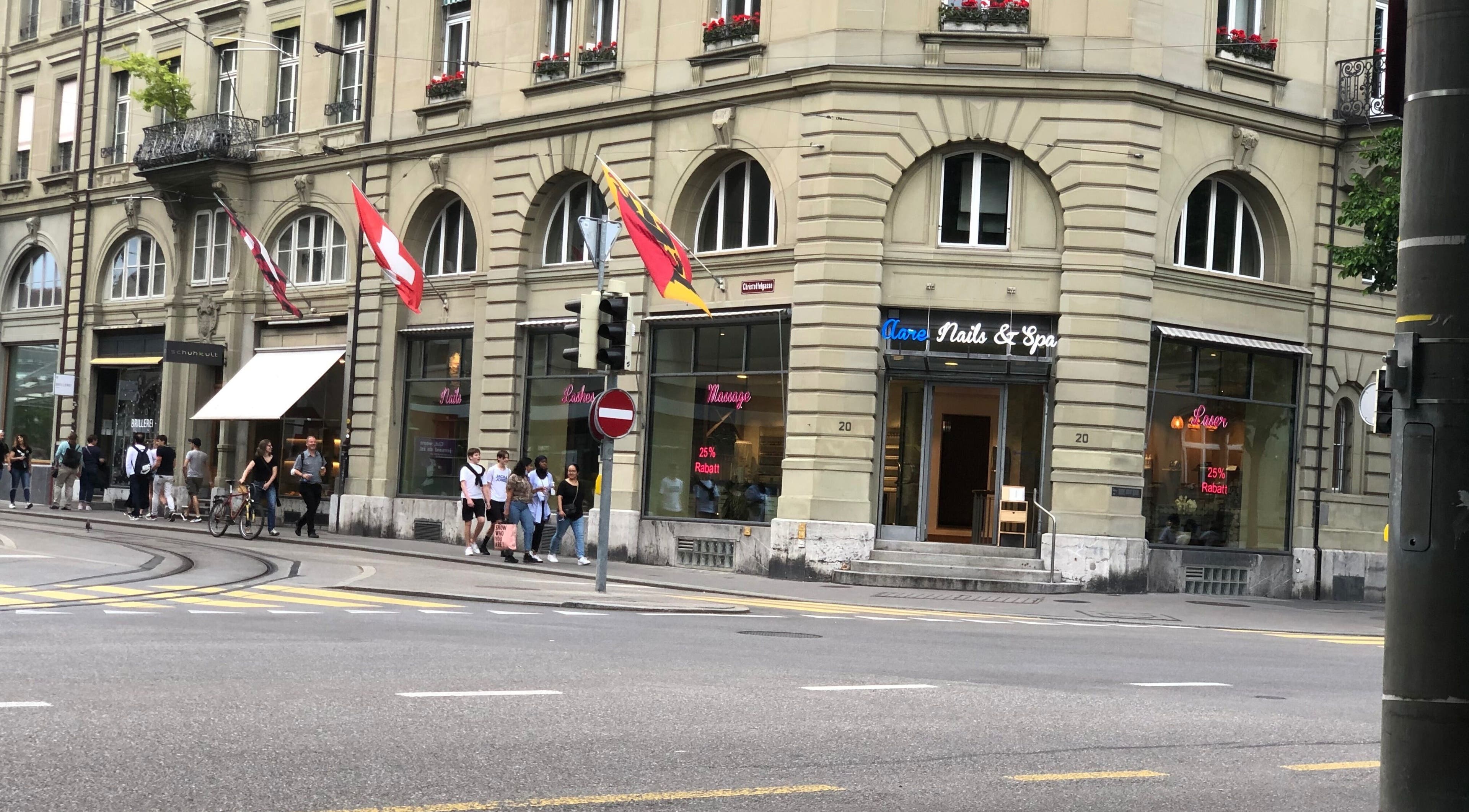 Eingang von Aare Nails & Spa, Bern, Bern, CH mit eleganter Fassade und Schweizer Flaggen im Hintergrund.
