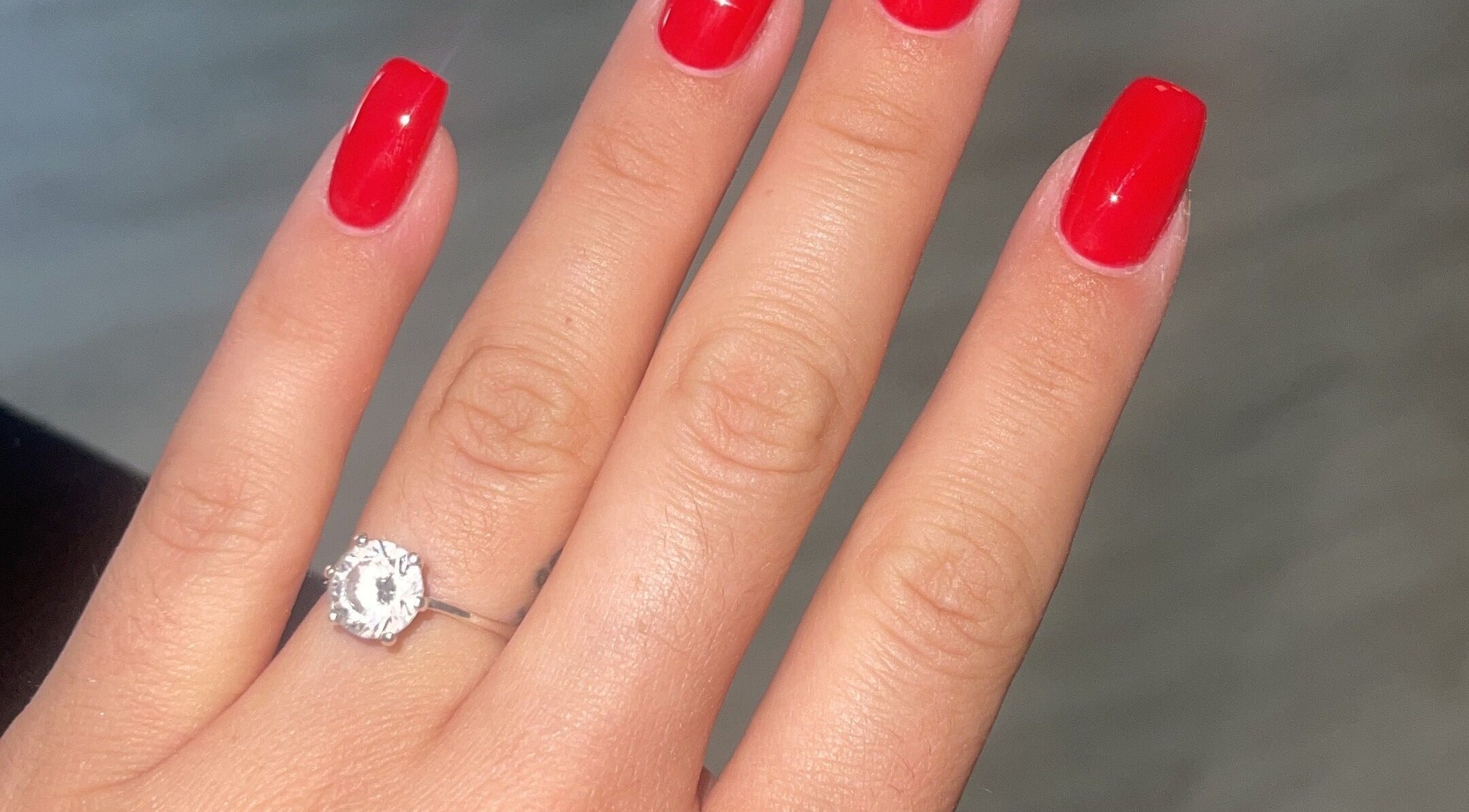 Elegant red manicured nails with a diamond ring at Demis Beauty, London, England, GB.