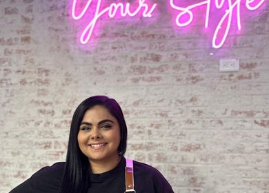 Mujer sonriente en Cosmetiando Medellín, Antioquia, CO, con letrero de neón en la pared de fondo.