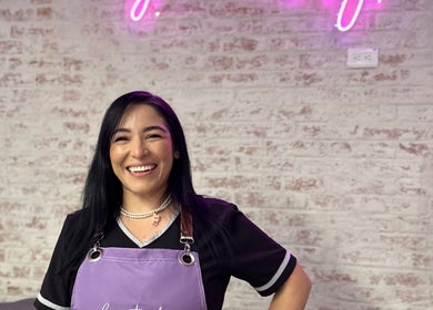 Profesional sonriente en Cosmetiando, Medellín, Antioquia, CO, con fondo de pared de ladrillo y neón.