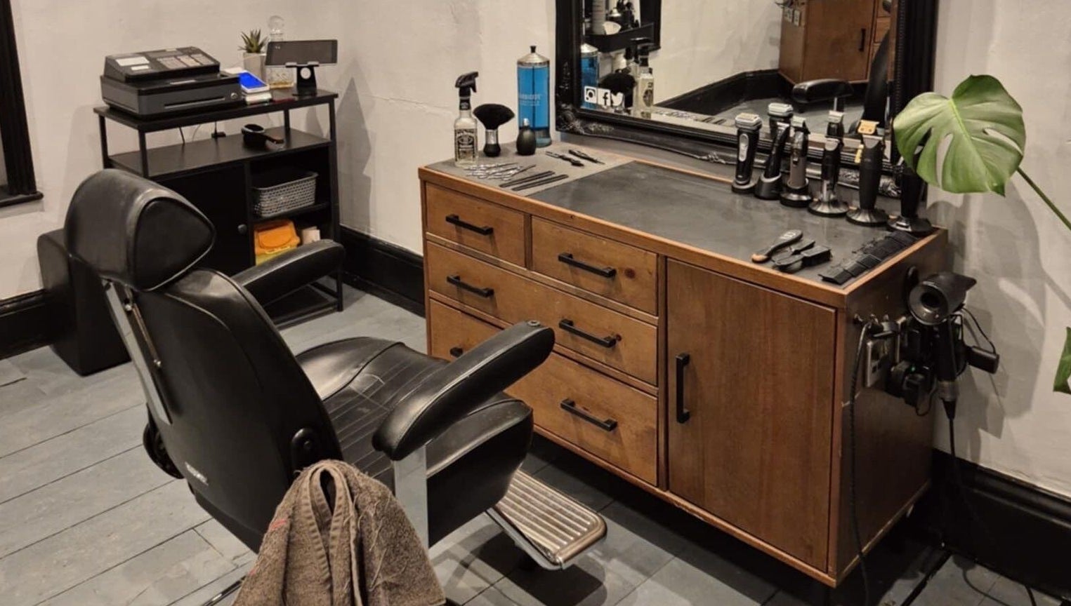 Elegant barber station at The Attic Barbershop in Norwich, England featuring sleek black chair and wooden counter.