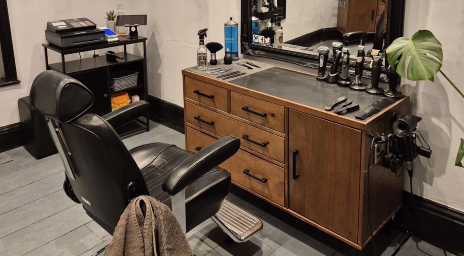 Elegant barber station at The Attic Barbershop in Norwich, England featuring sleek black chair and wooden counter.