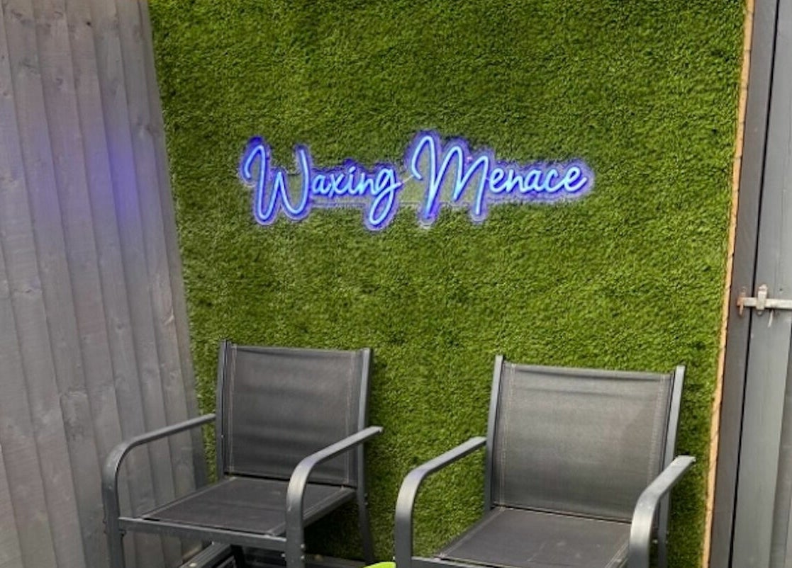 Chic seating area at The Waxing Menace, Stevenage, England, GB, featuring stylish chairs and lush green backdrop.