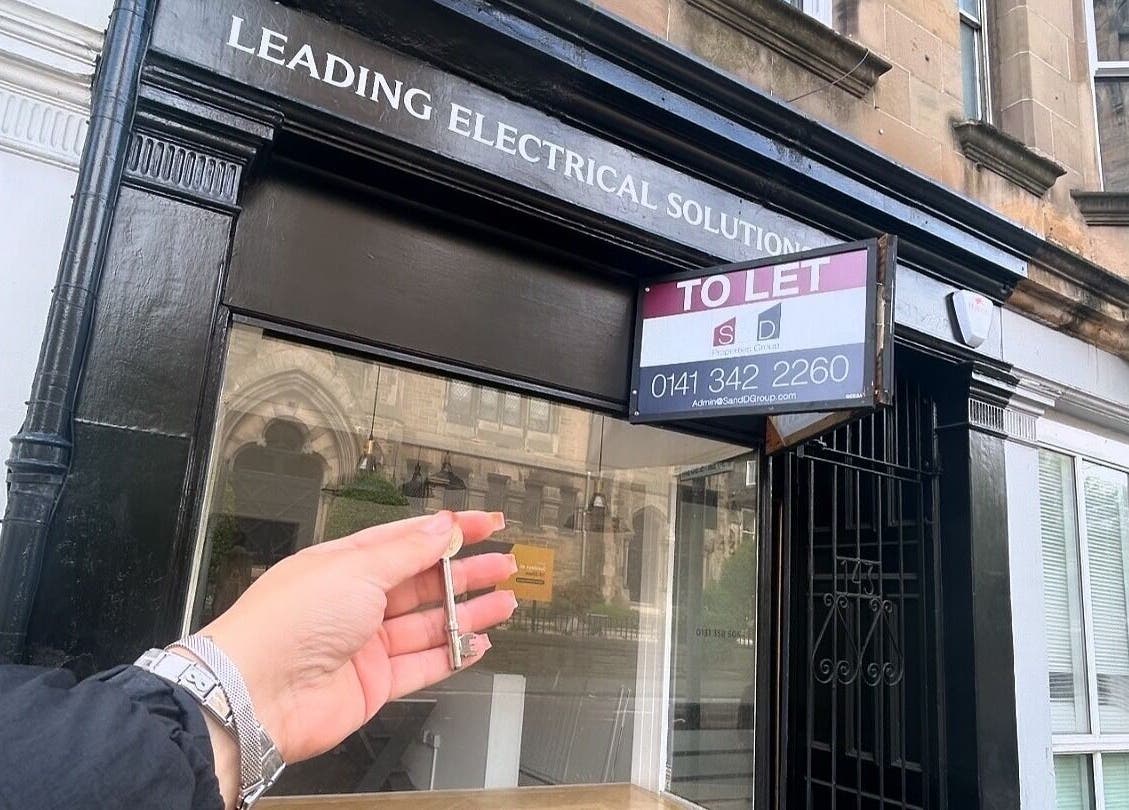 Hand holding key in front of Lashmek location, Edinburgh, Scotland, GB under a 'To Let' sign.