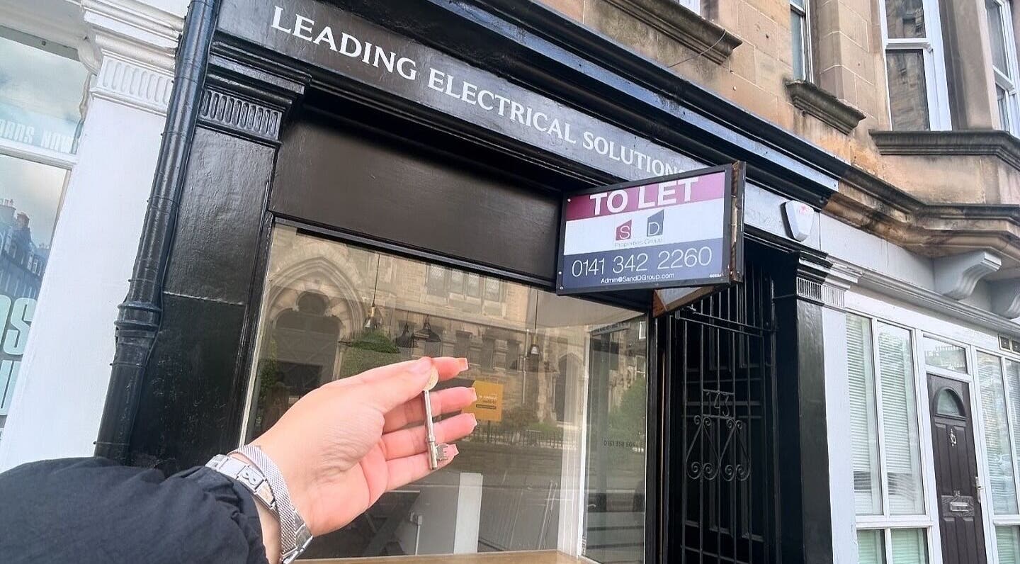 Hand holding key in front of Lashmek location, Edinburgh, Scotland, GB under a 'To Let' sign.