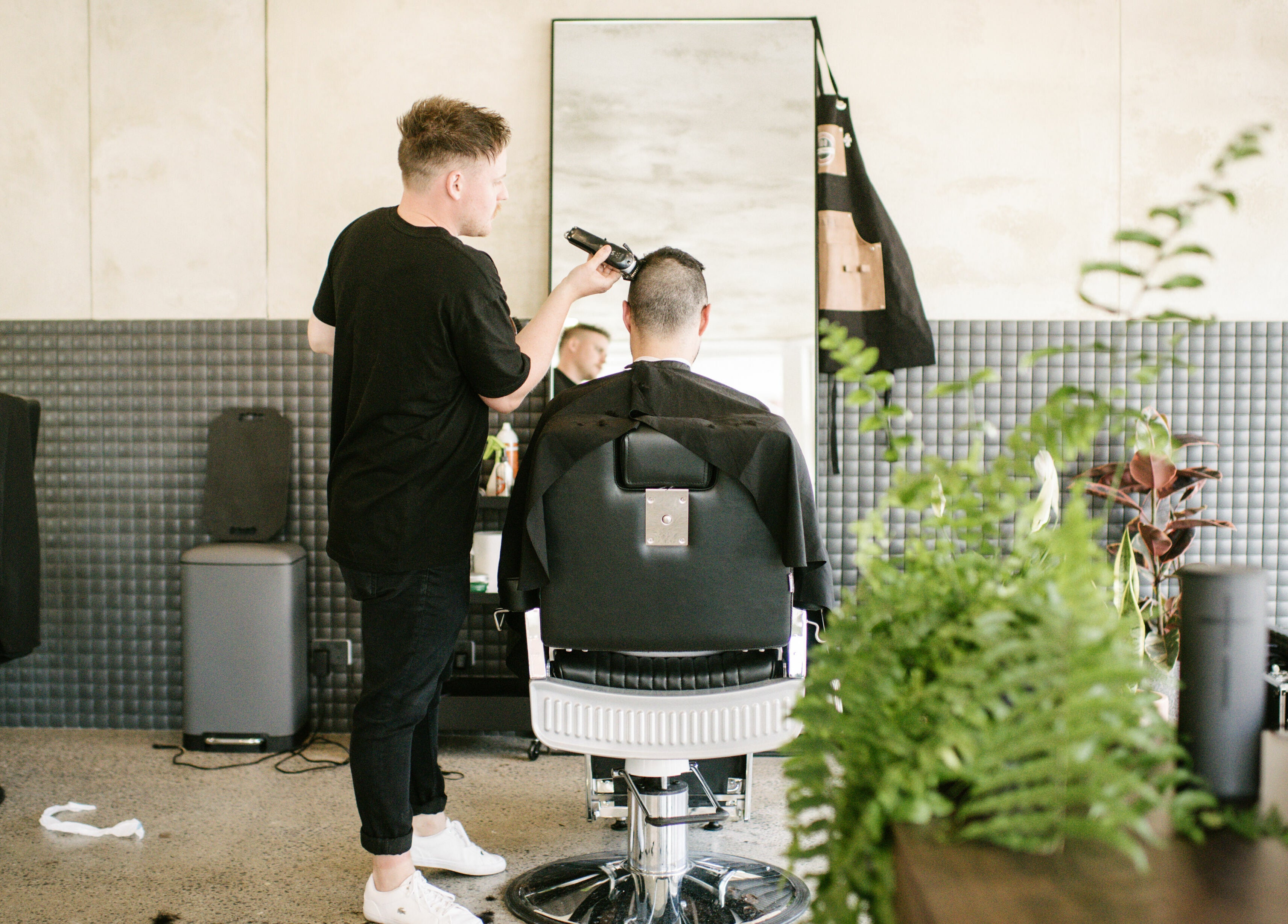 Barber styling client at Eastside, Camberwell, VIC, AU amidst modern decor and vibrant plants.