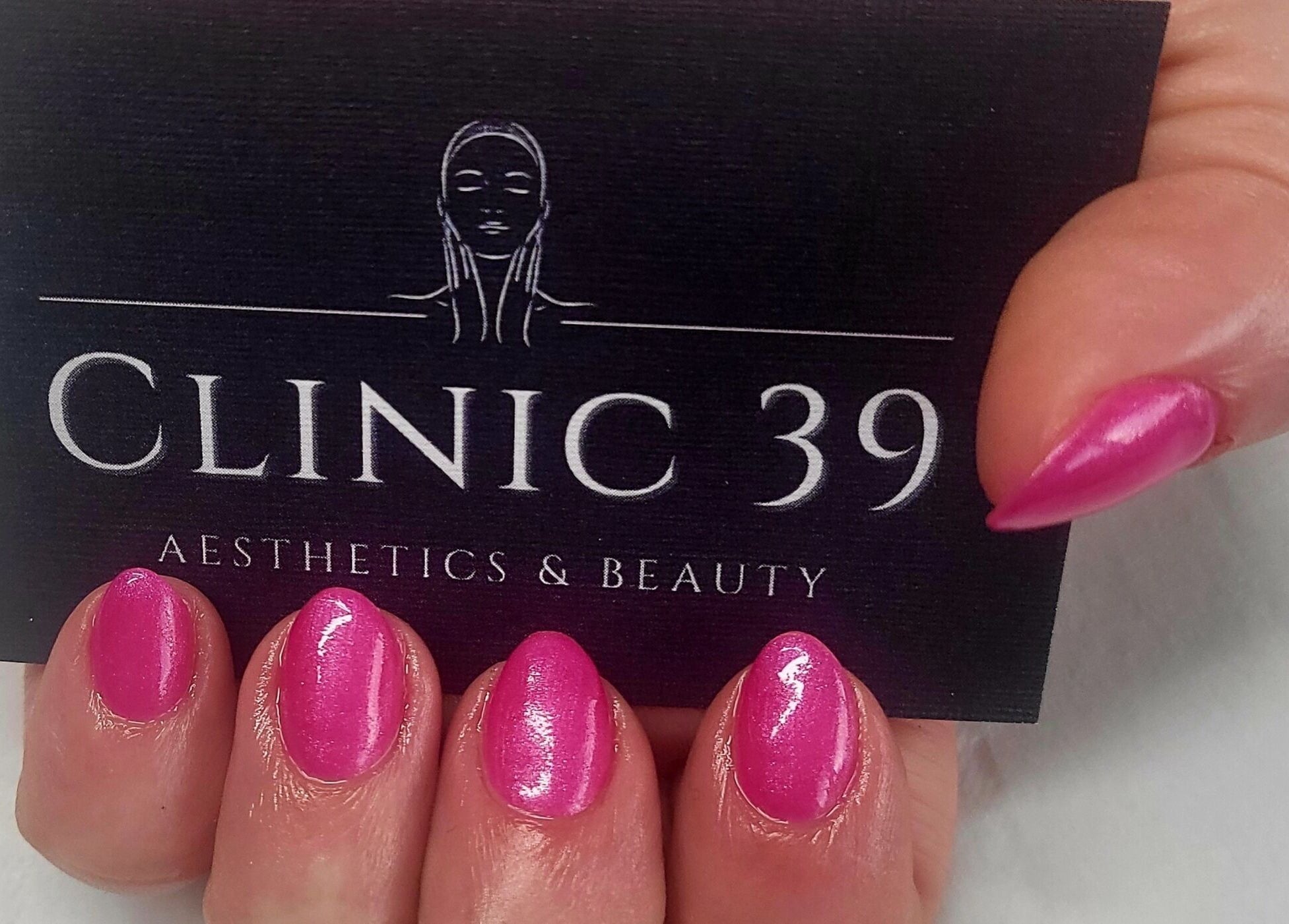Pink manicured nails holding Clinic 39 Aesthetics & Beauty card in Swansea, Wales, GB.
