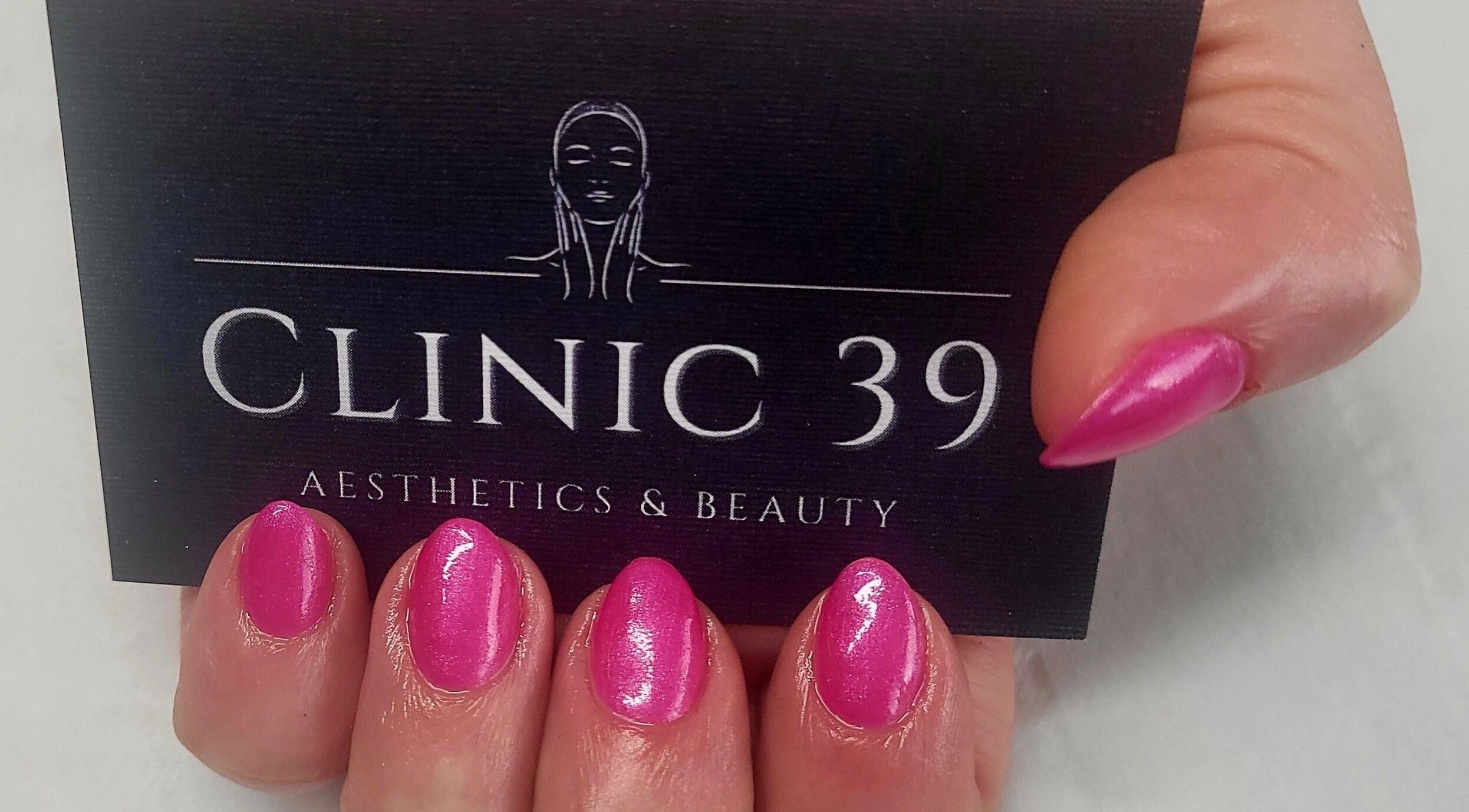 Pink manicured nails holding Clinic 39 Aesthetics & Beauty card in Swansea, Wales, GB.