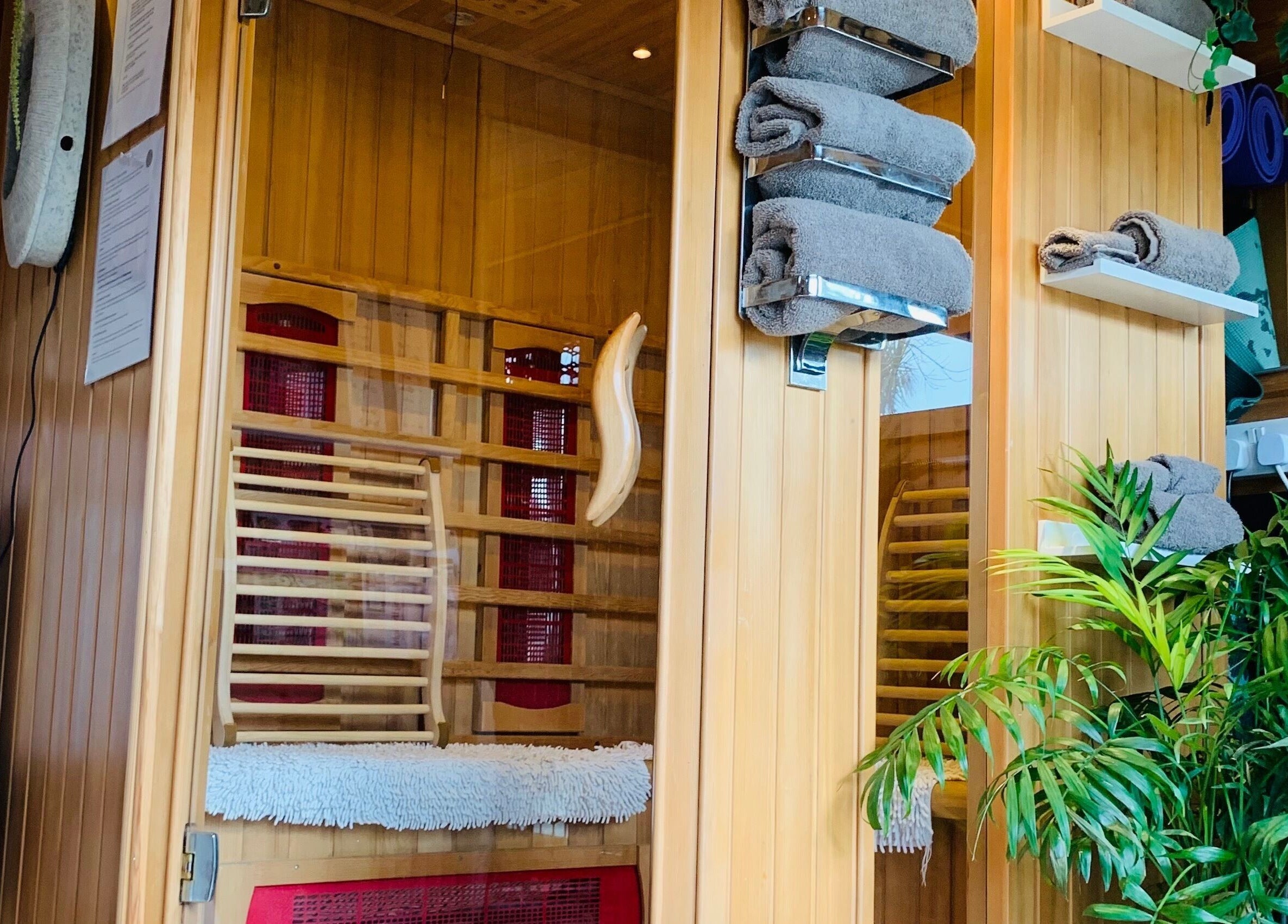 Warm wooden sauna interior at Pure Calma Healing, Bournemouth, England, GB with lush greenery and soft towels.