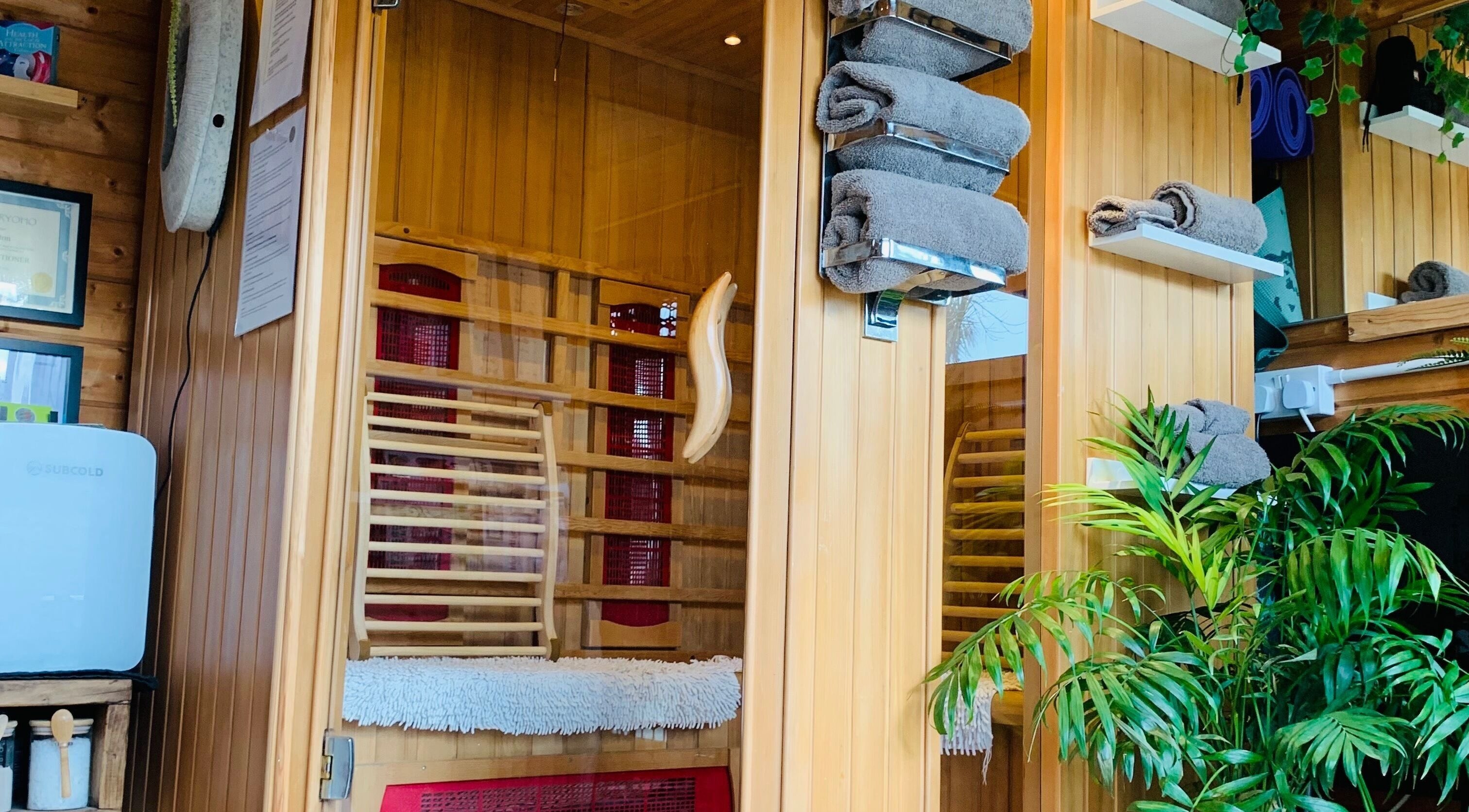 Warm wooden sauna interior at Pure Calma Healing, Bournemouth, England, GB with lush greenery and soft towels.