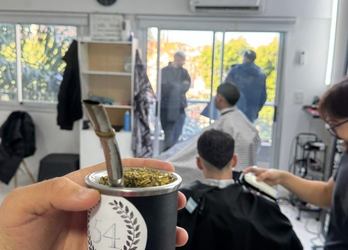 Interior de ESTUDIO 54 en Buenos Aires, con cliente recibiendo corte de cabello mientras se toma mate.
