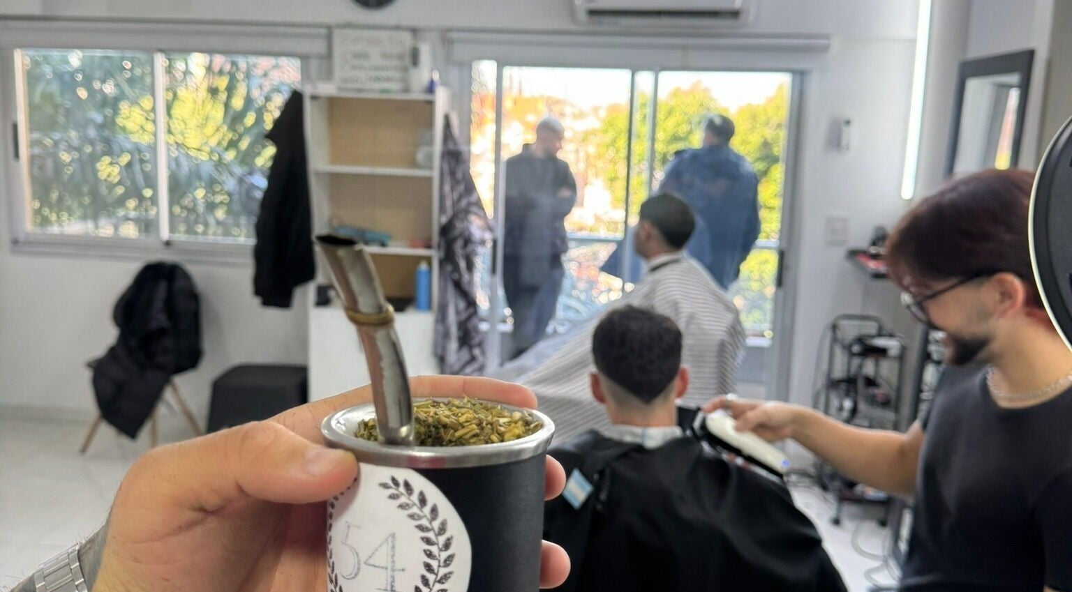 Interior de ESTUDIO 54 en Buenos Aires, con cliente recibiendo corte de cabello mientras se toma mate.