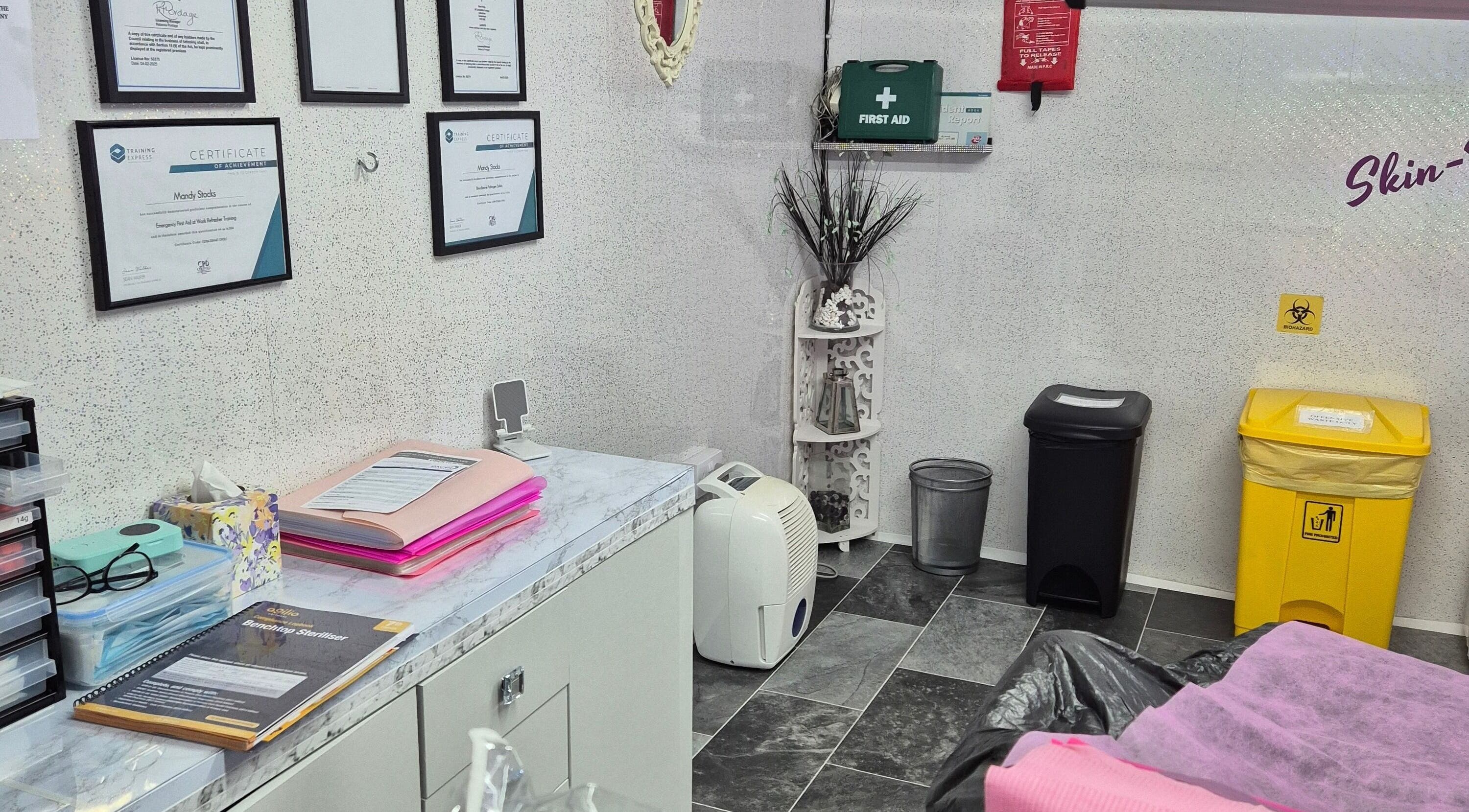 Skin-Finity treatment room in Aylesham, England, featuring certificates and essential supplies.