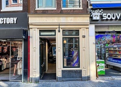 Entrance of Prime Barbershop Amsterdam, nestled between shops in Amsterdam, Noord-Holland, NL.