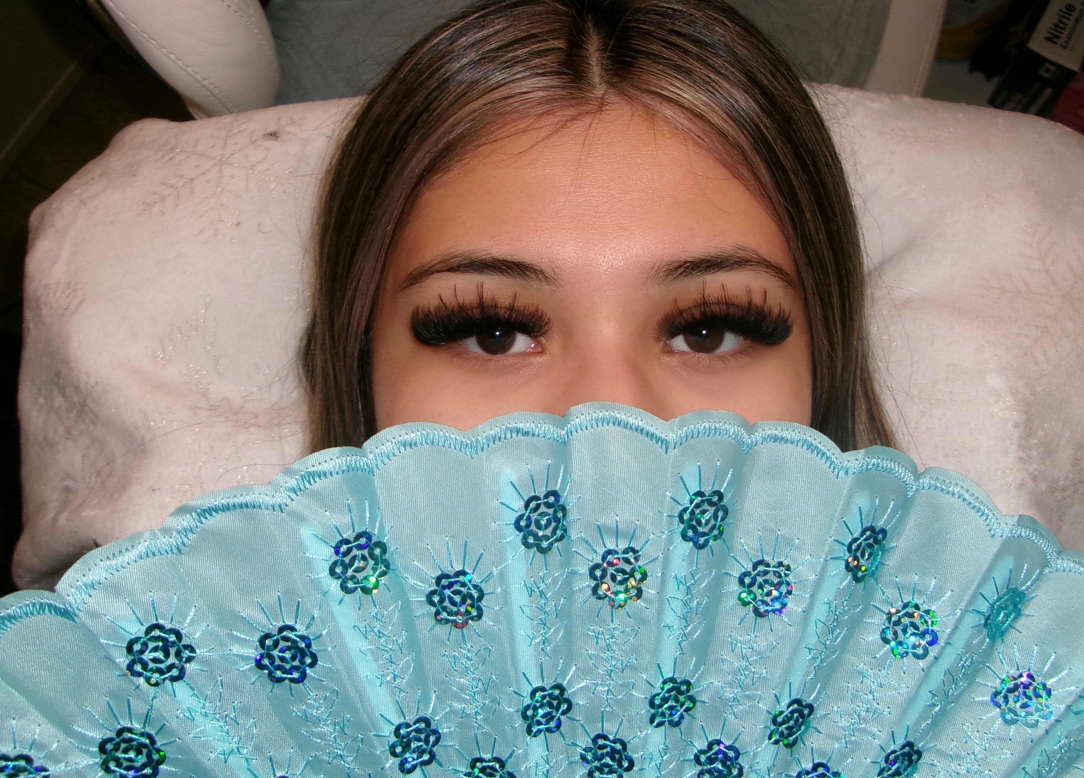 Woman with elegant lashes and blue fan at Icey Pearlz, Catoosa, Oklahoma, US.
