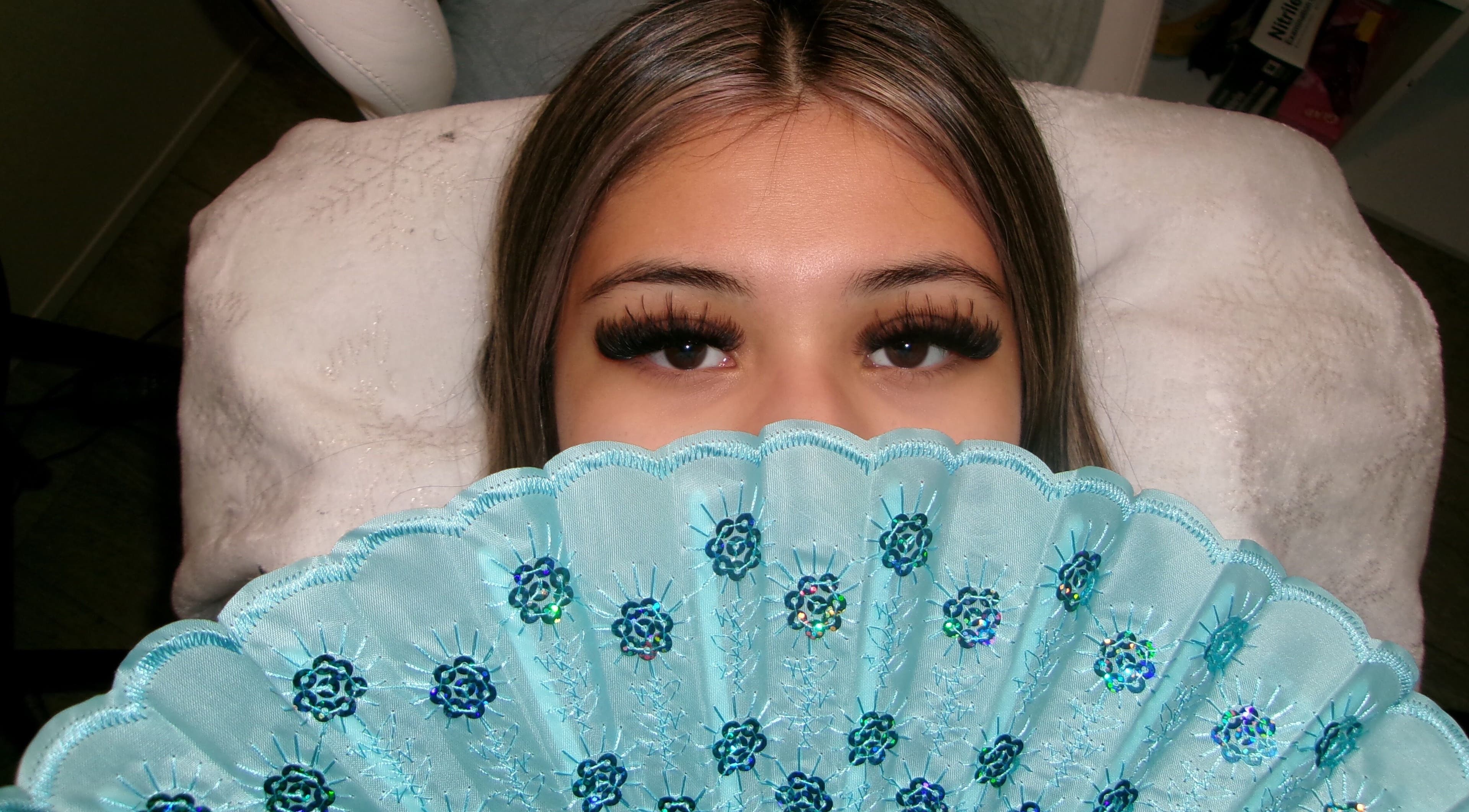 Woman with elegant lashes and blue fan at Icey Pearlz, Catoosa, Oklahoma, US.