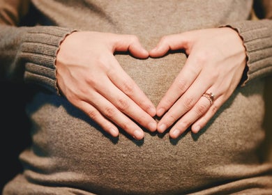 Close-up of pregnant belly with heart hands at Boutique Massage Studios, Meadow Springs, Western Australia, AU.