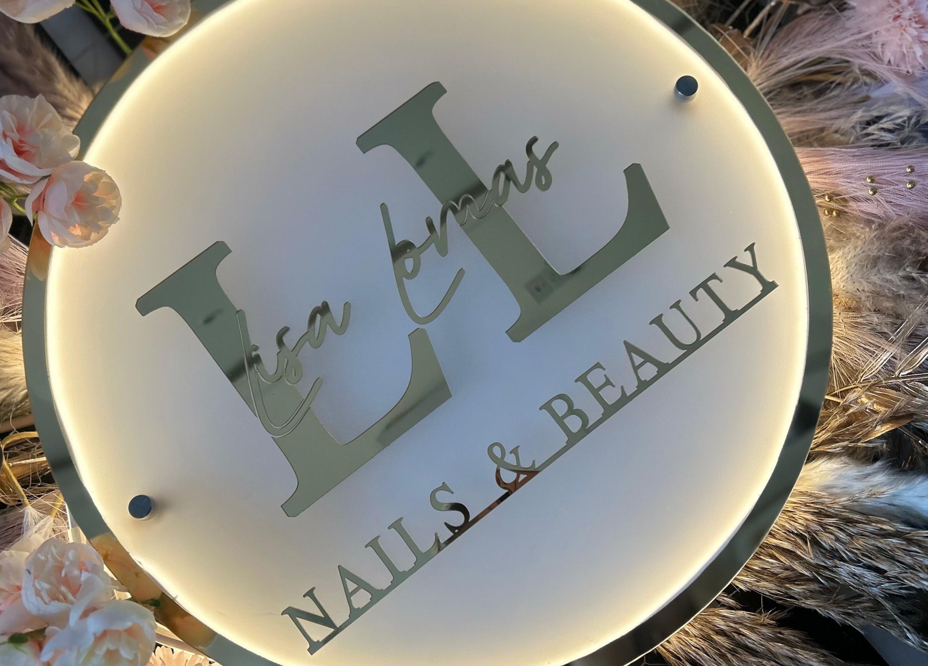 Illuminated sign of Lisa Lomas Nails and Beauty in Blackpool, England, GB surrounded by pink flowers.