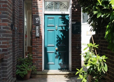 Charming teal door at Big Calm Reflexology, London, England, GB, surrounded by bricks and lush greenery.
