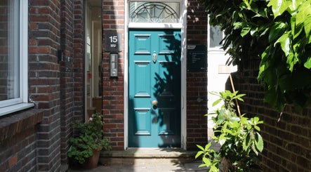 Charming teal door at Big Calm Reflexology, London, England, GB, surrounded by bricks and lush greenery.