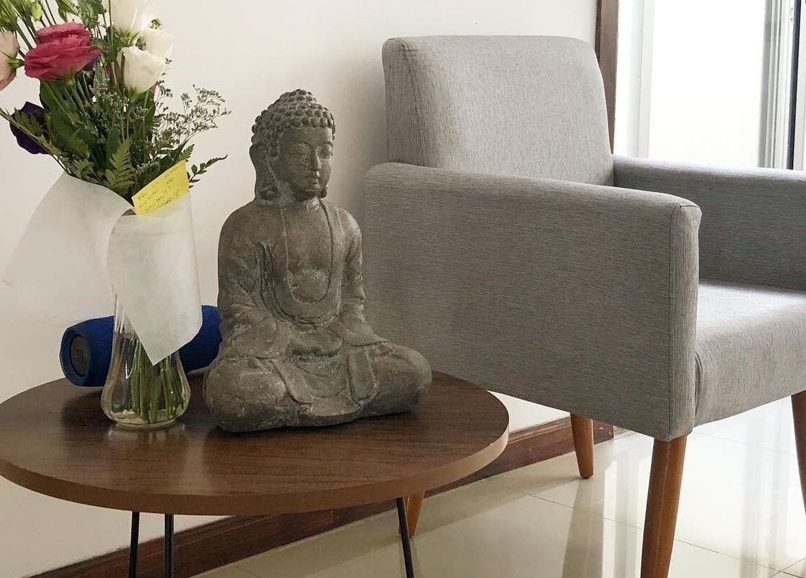 Estatua de Buda en mesa junto a silla gris en Samadhi, Montevideo, Departamento De Montevideo, UY.