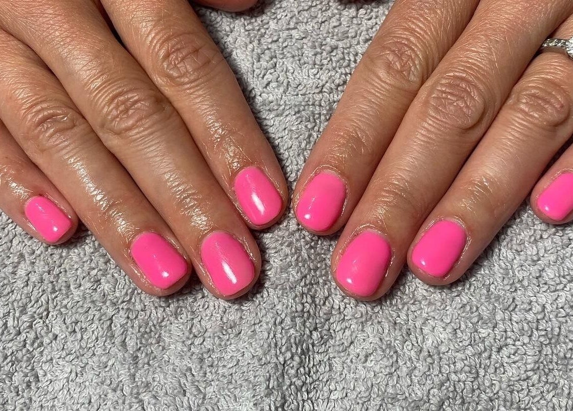 Vibrant pink manicure at JD Nails, Telford, England, GB. Perfectly polished fingernails on a soft towel.