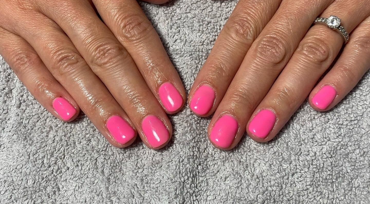 Vibrant pink manicure at JD Nails, Telford, England, GB. Perfectly polished fingernails on a soft towel.