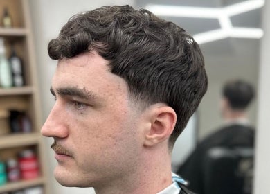 Modern men's haircut at Quinche Studio, Mascot, New South Wales, AU. Sleek, stylish look with a barber in the background.