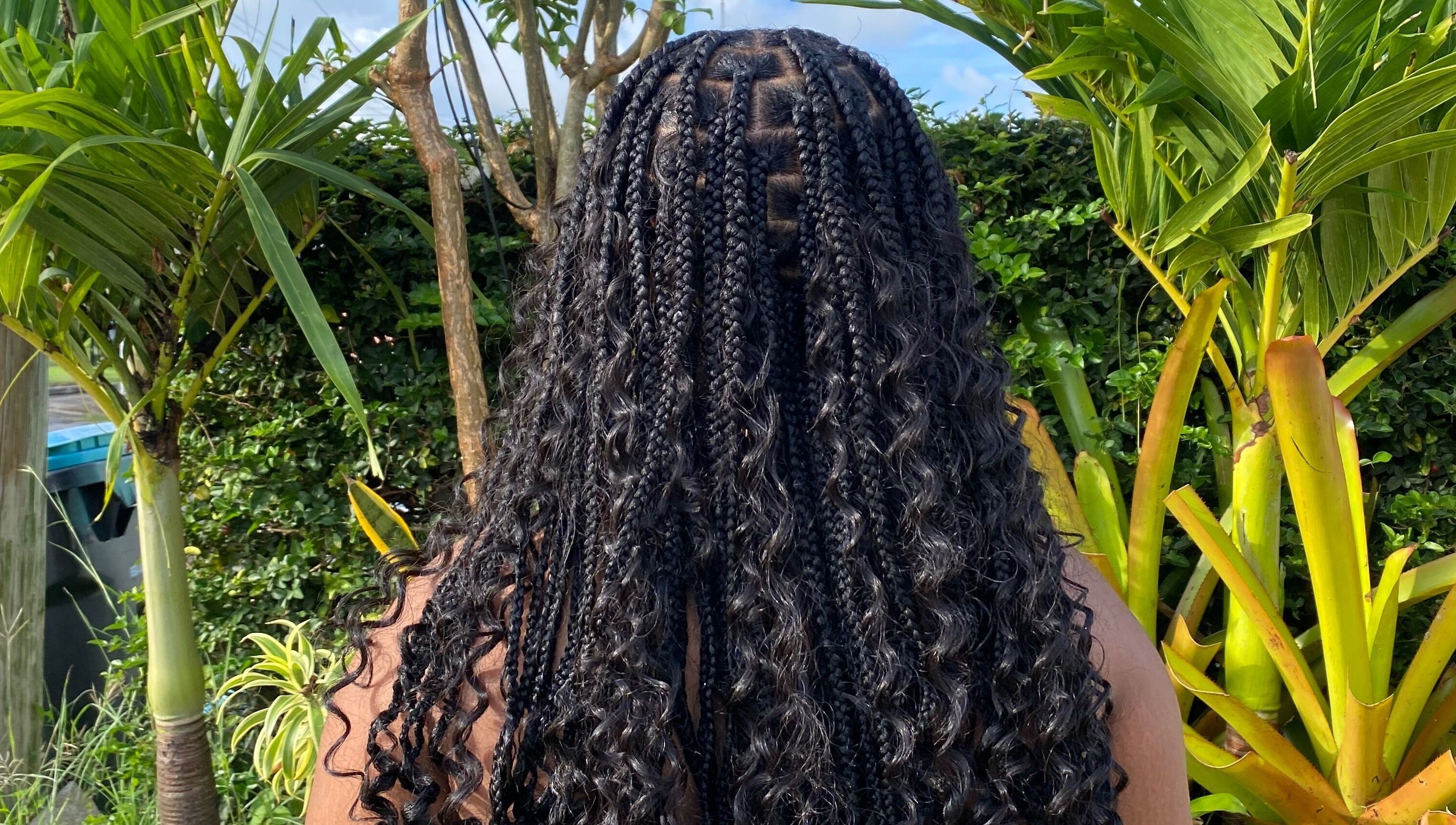 Braided hairstyle showcased at Flux Beauty, Oistins, Christ Church, BB with lush greenery in the background.