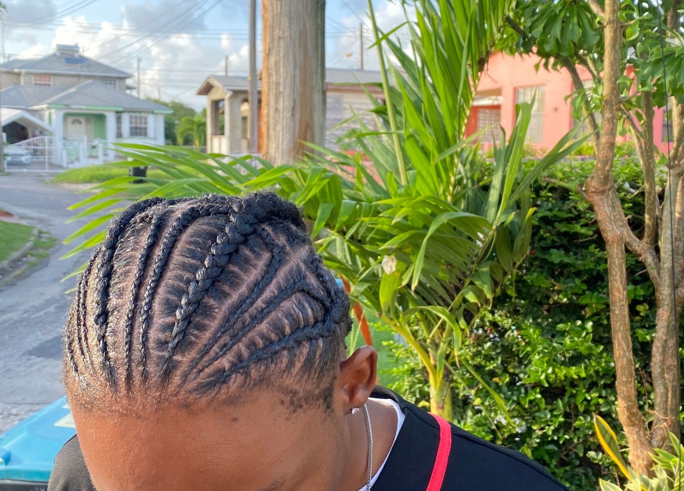 Intricate cornrow hairstyle showcased at Flux Beauty, Oistins, Christ Church, BB, surrounded by lush greenery.