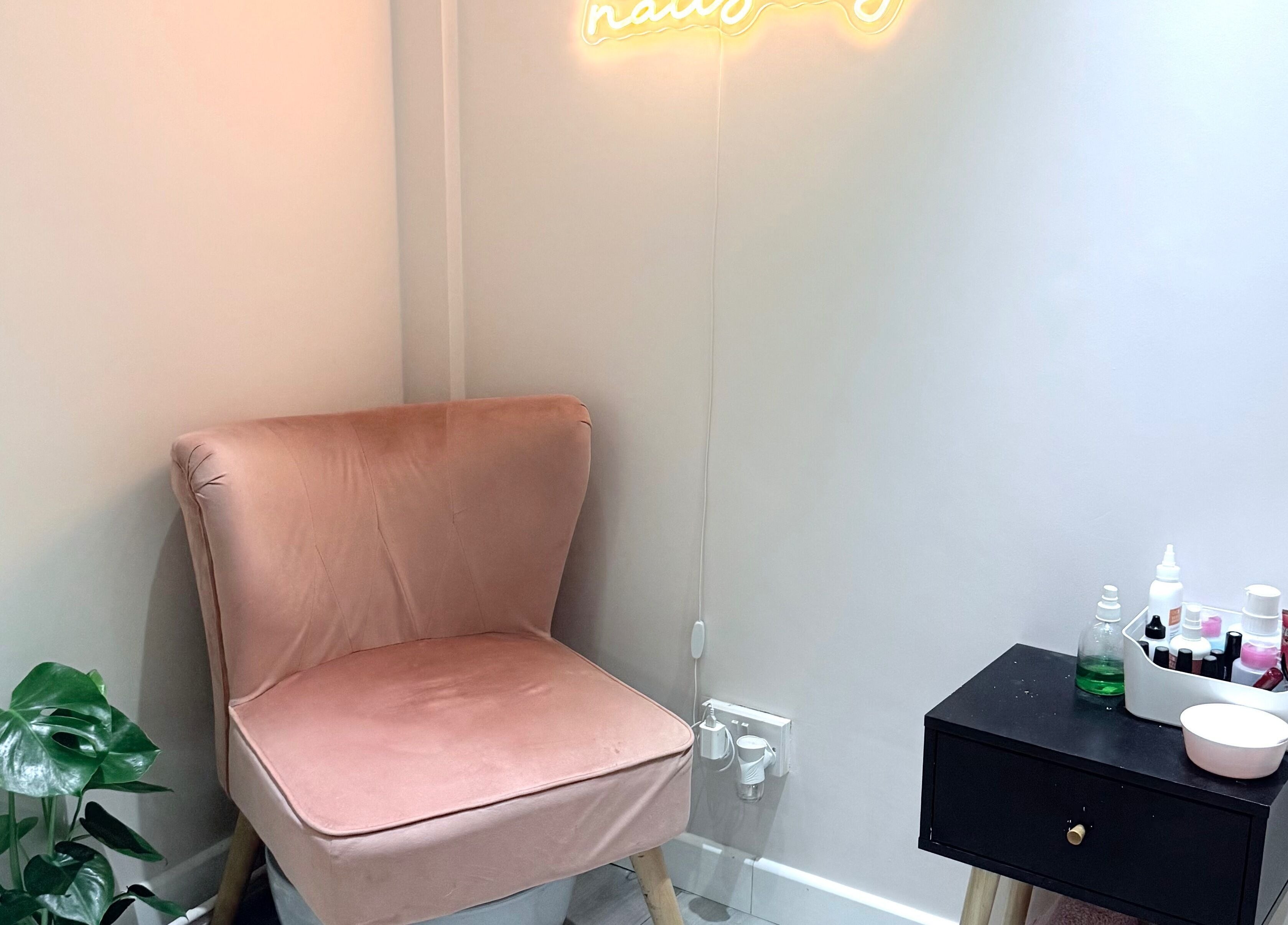 Cozy corner at Ashley Blakemore Beauty & PMU, Cheadle, with a pink chair, neon sign, and product table.