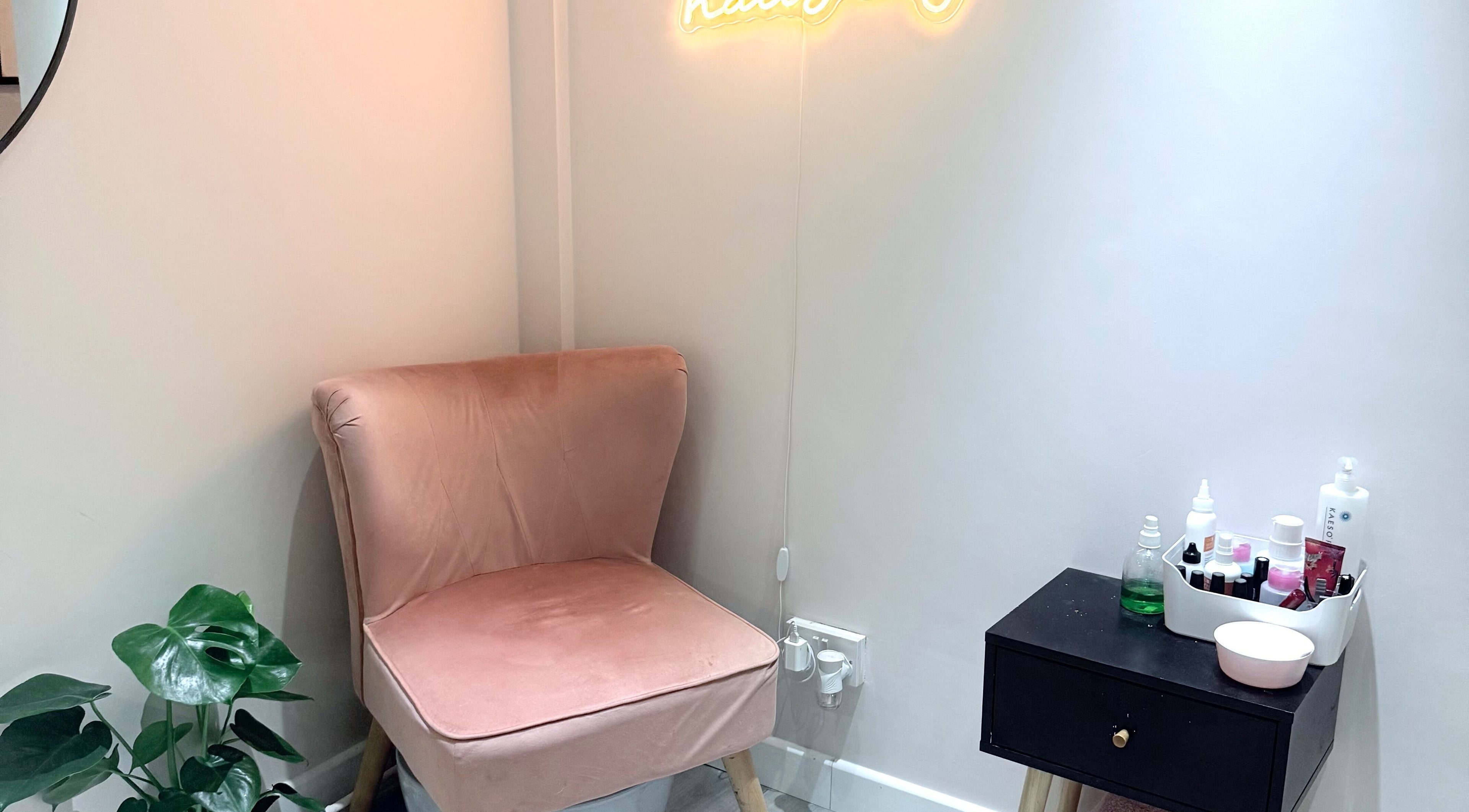 Cozy corner at Ashley Blakemore Beauty & PMU, Cheadle, with a pink chair, neon sign, and product table.