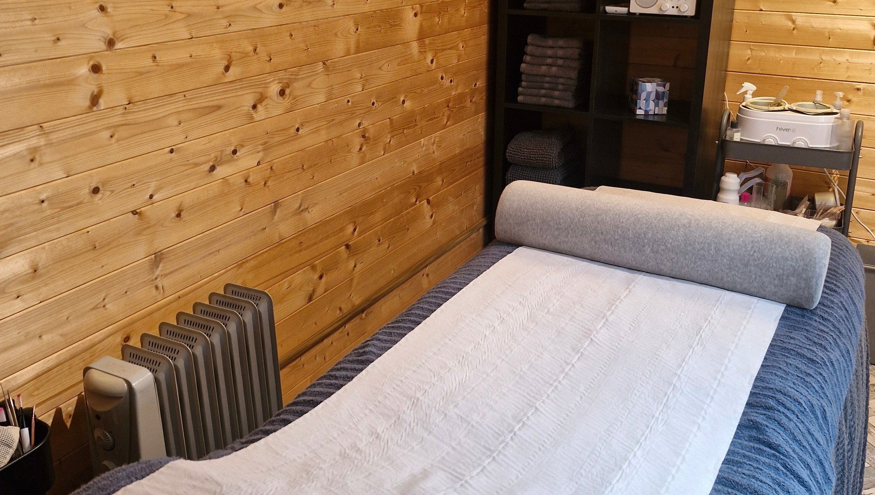Massage room at Bare Essential Beauty, Addington, England, featuring a wooden interior and cozy massage bed.